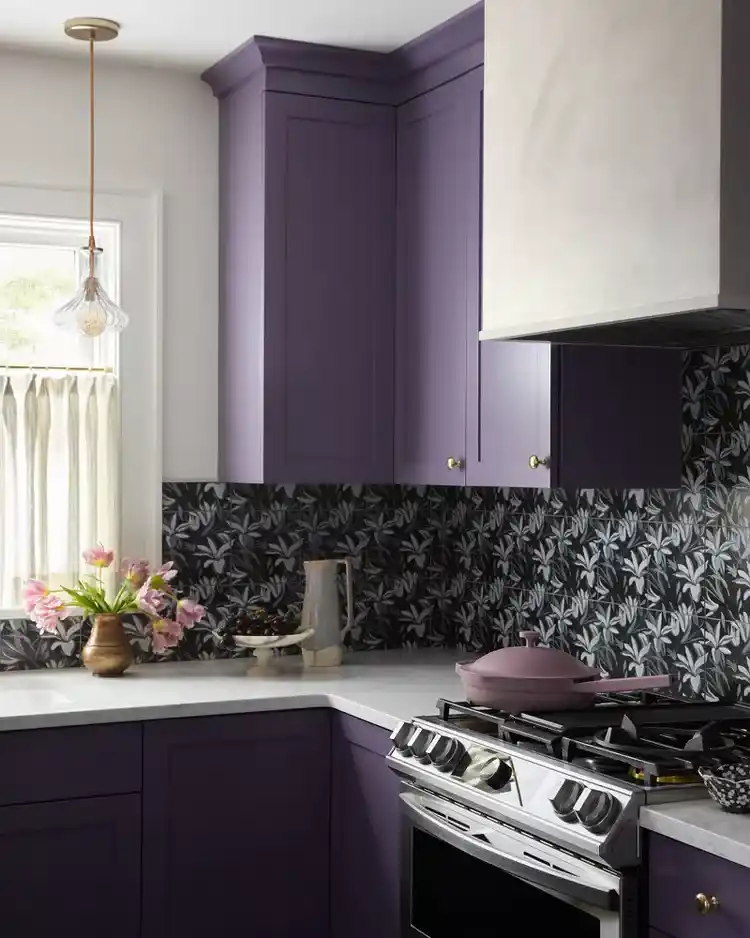 Black and white kitchen backsplash with delicate white floral patterns on black tiles and purple cabinets