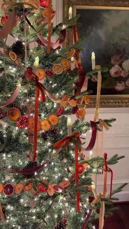 Orange garland on a Christmas tree with ribbons and candles.